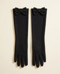 Pair of long black gloves with a bow at the top cuff on a cream studio backdrop