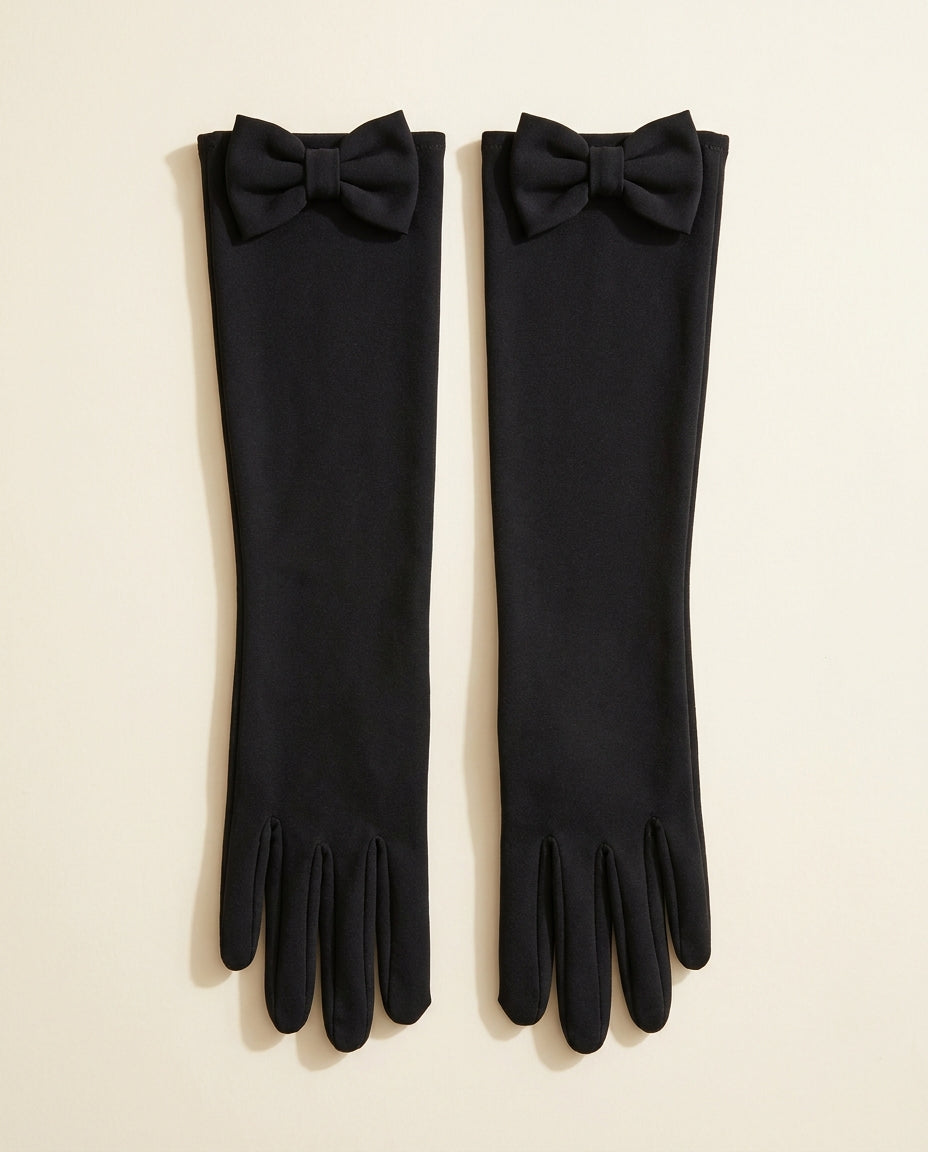 Pair of long black gloves with a bow at the top cuff on a cream studio backdrop