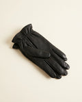 Pair of sleek black gloves with a gathered ruched wrist on a cream studio backdrop