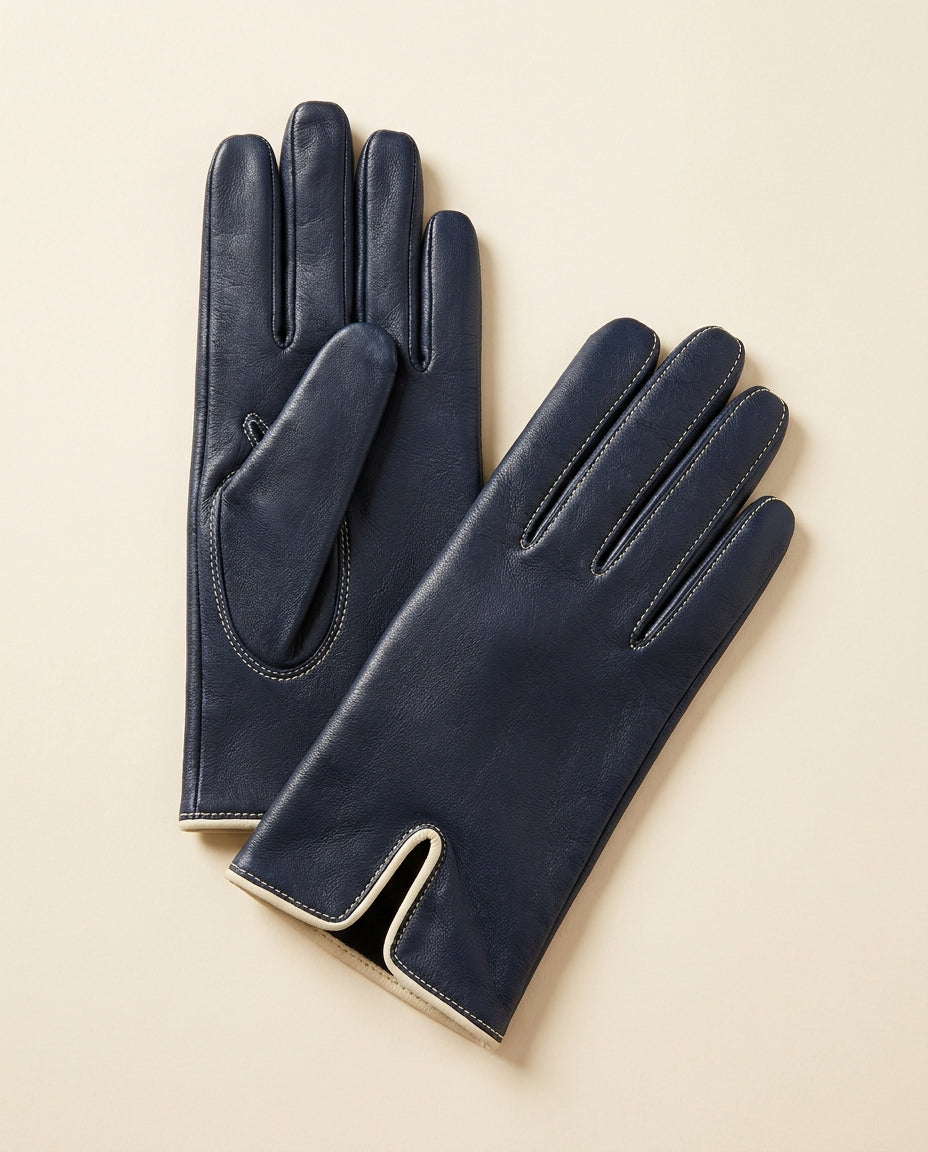 Pair of navy driving gloves with cream trim on a cream studio backdrop