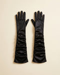 Pair of long black gloves ruched along the arm on a cream studio backdrop