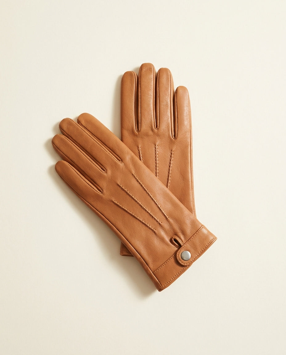 Pair of tan driving gloves with topstitching and a wrist snap on a cream studio backdrop