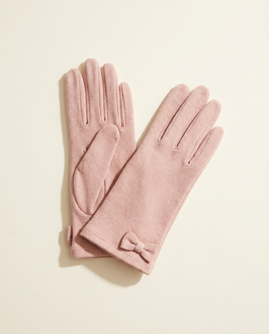 Pair of blush pink gloves with a small bow at the wrist on a cream studio backdrop