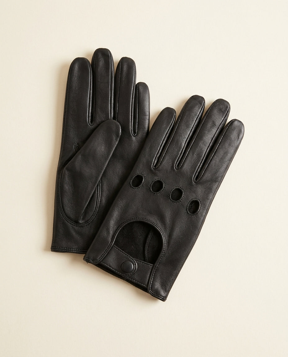 Pair of black open-knuckle driving gloves with a snap strap on a cream studio backdrop