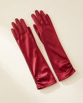 Pair of deep red gathered evening gloves with a soft sheen on a cream studio backdrop